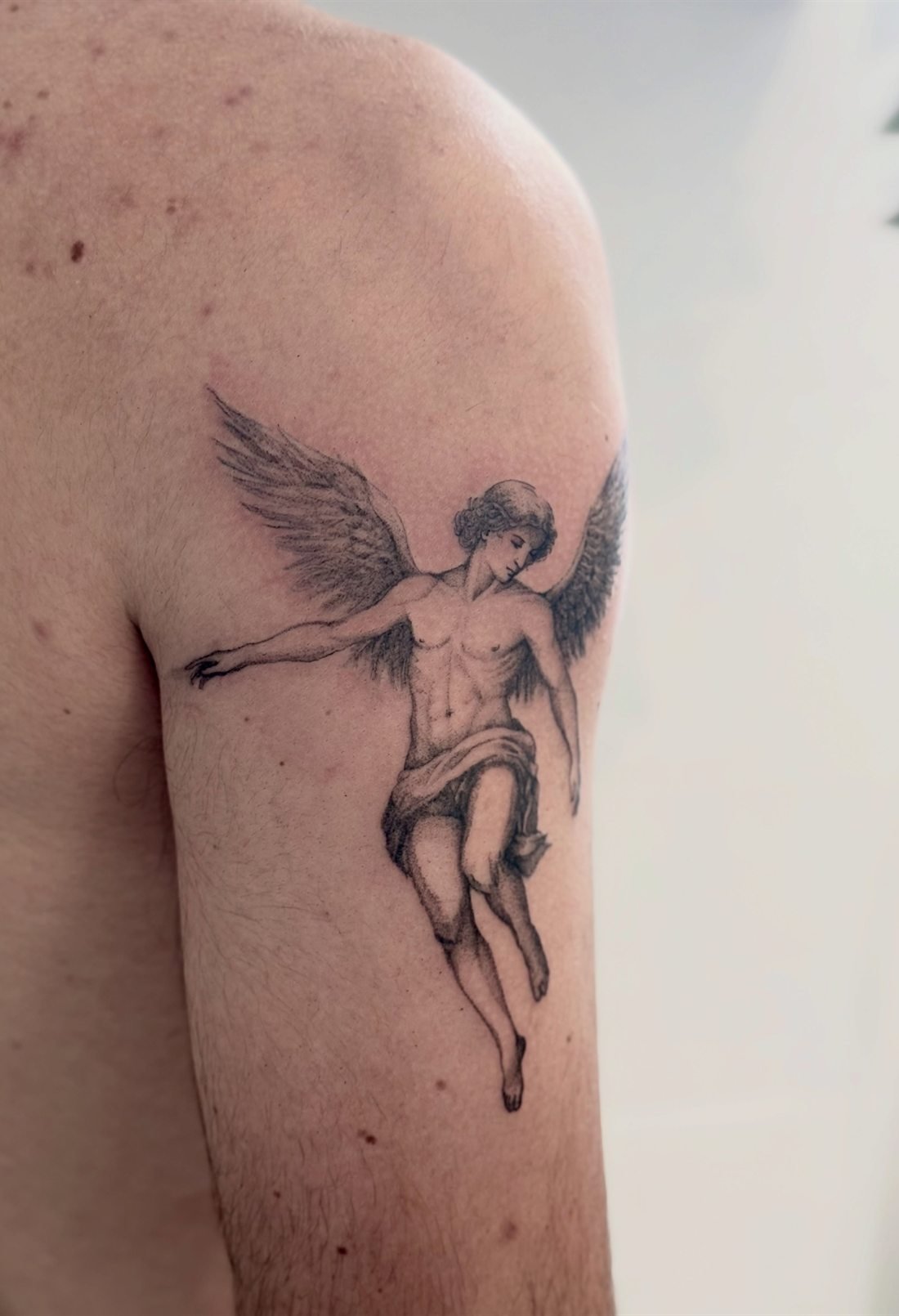 Tatouage d’une figure ailée descendant, réalisé en semi-réalisme sur l’épaule
